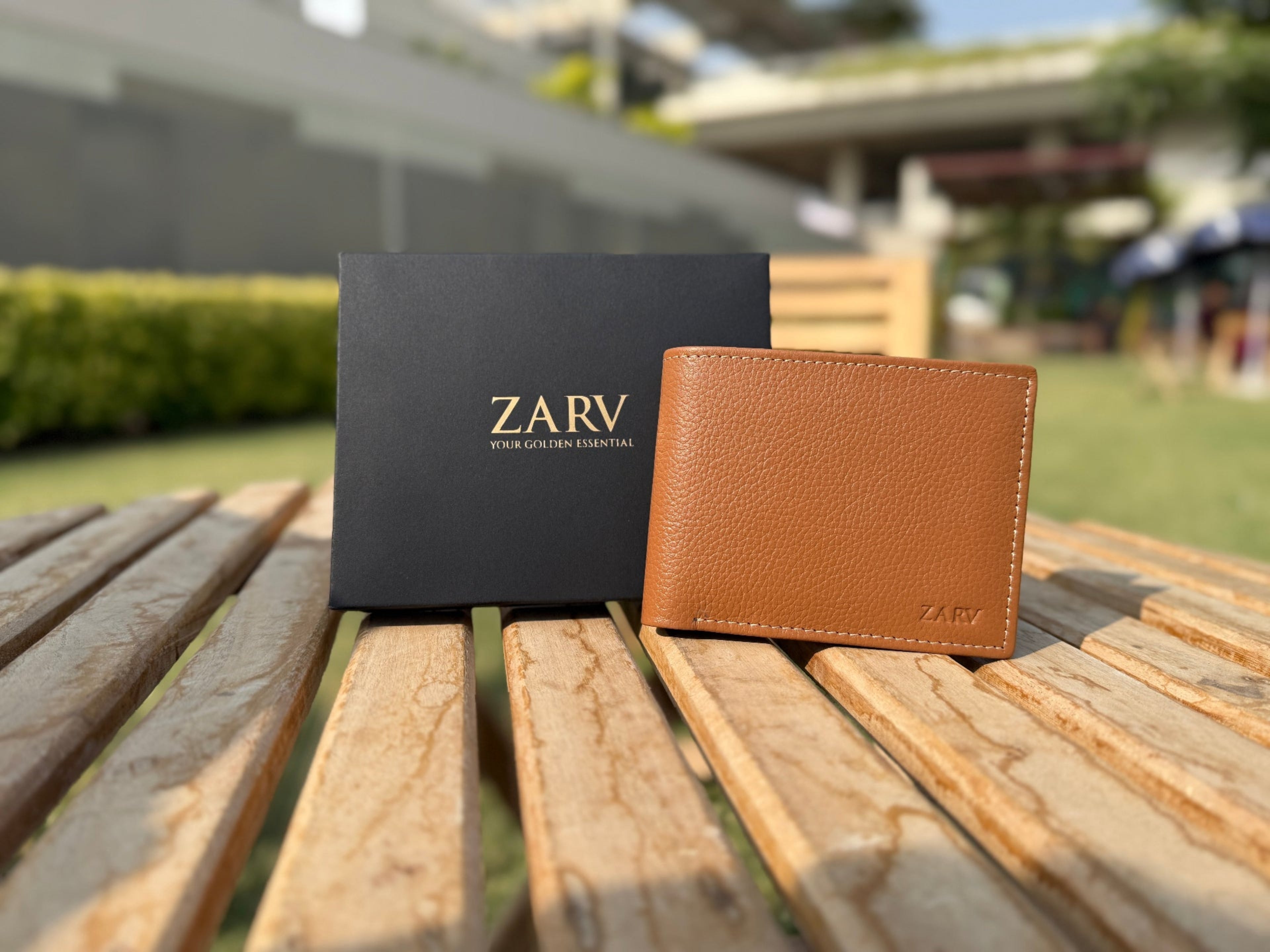 Tan leather wallet and black box with 'ZARV' branding on a wooden surface outdoors.