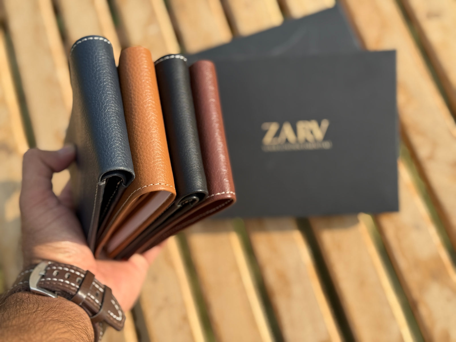 Four leather wallets in different colors held by a hand, with a 'ZARV' branded card in the background.