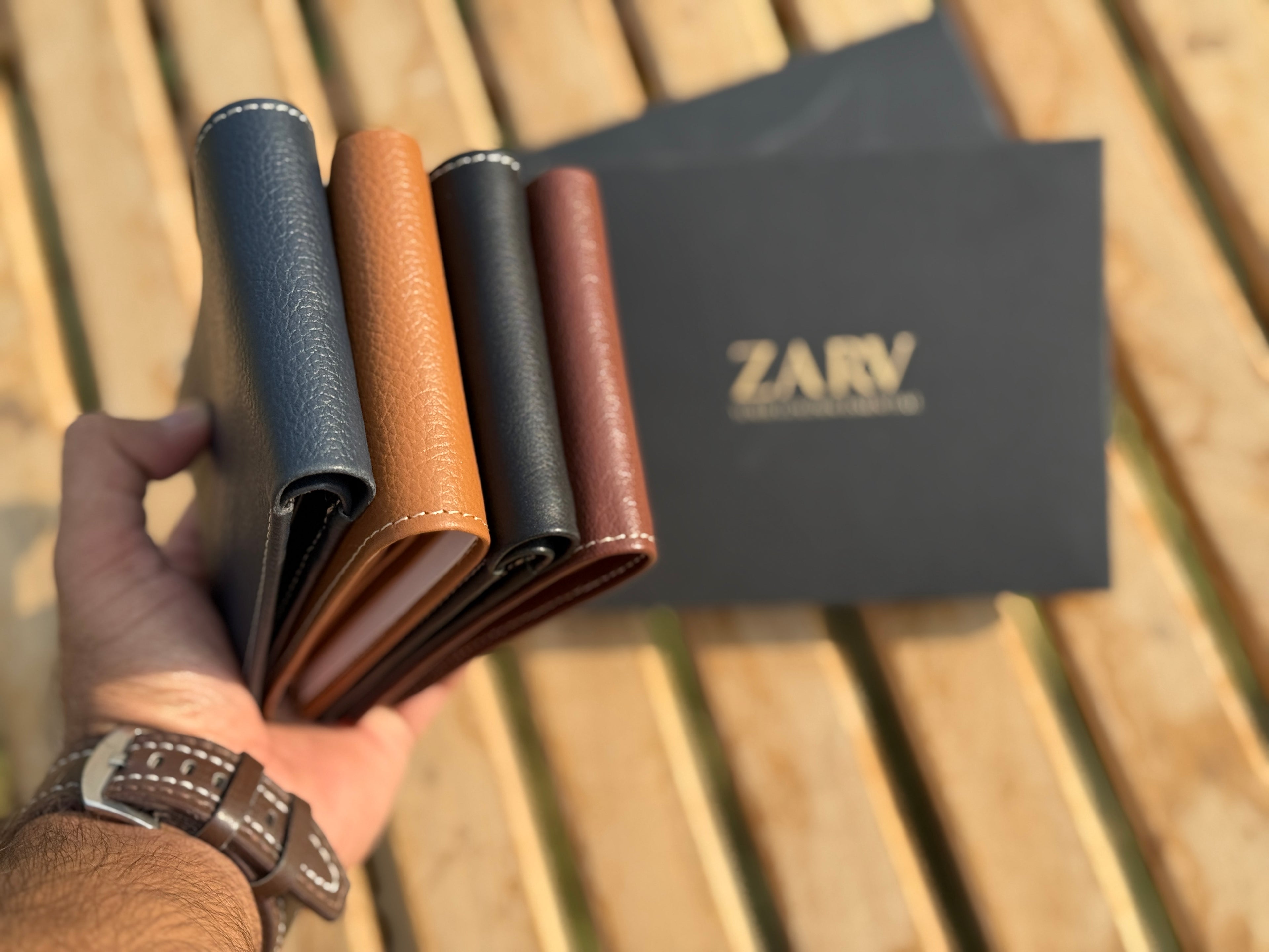 Four leather wallets in different colors held by a hand, with a 'ZARV' branded card in the background.
